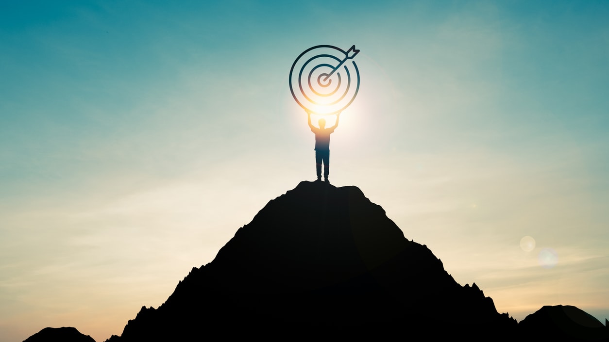 A silhouette of a man standing on top of a mountain with a target in his hand.