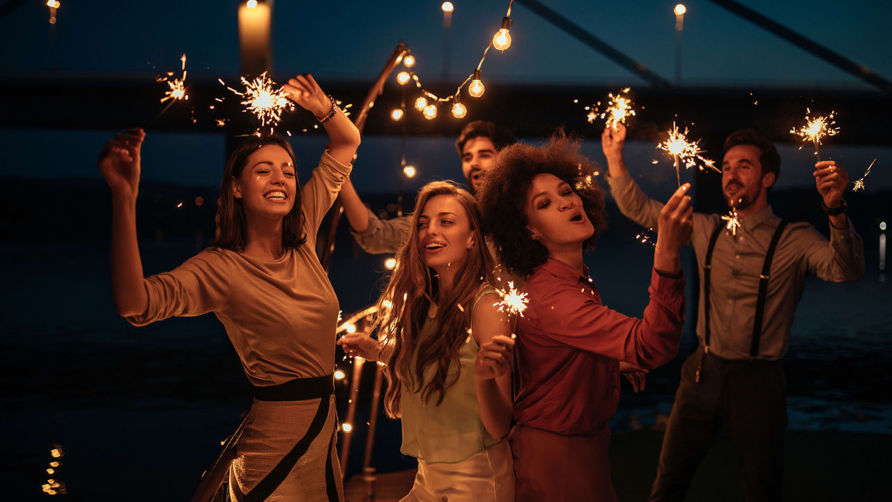 A group of friends holding sparklers on a dock.