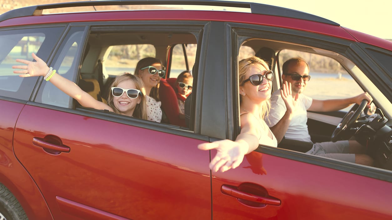 A group of people in a red car waving.