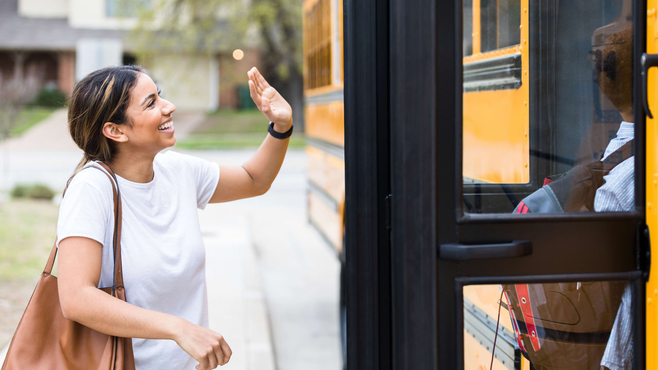 A young woman waving at a school bus.