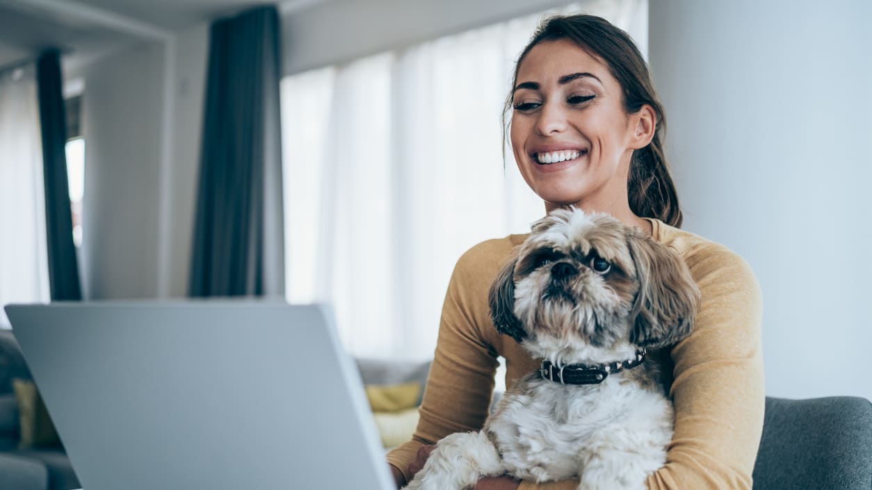 A woman with a dog sitting at a desk with a laptop.