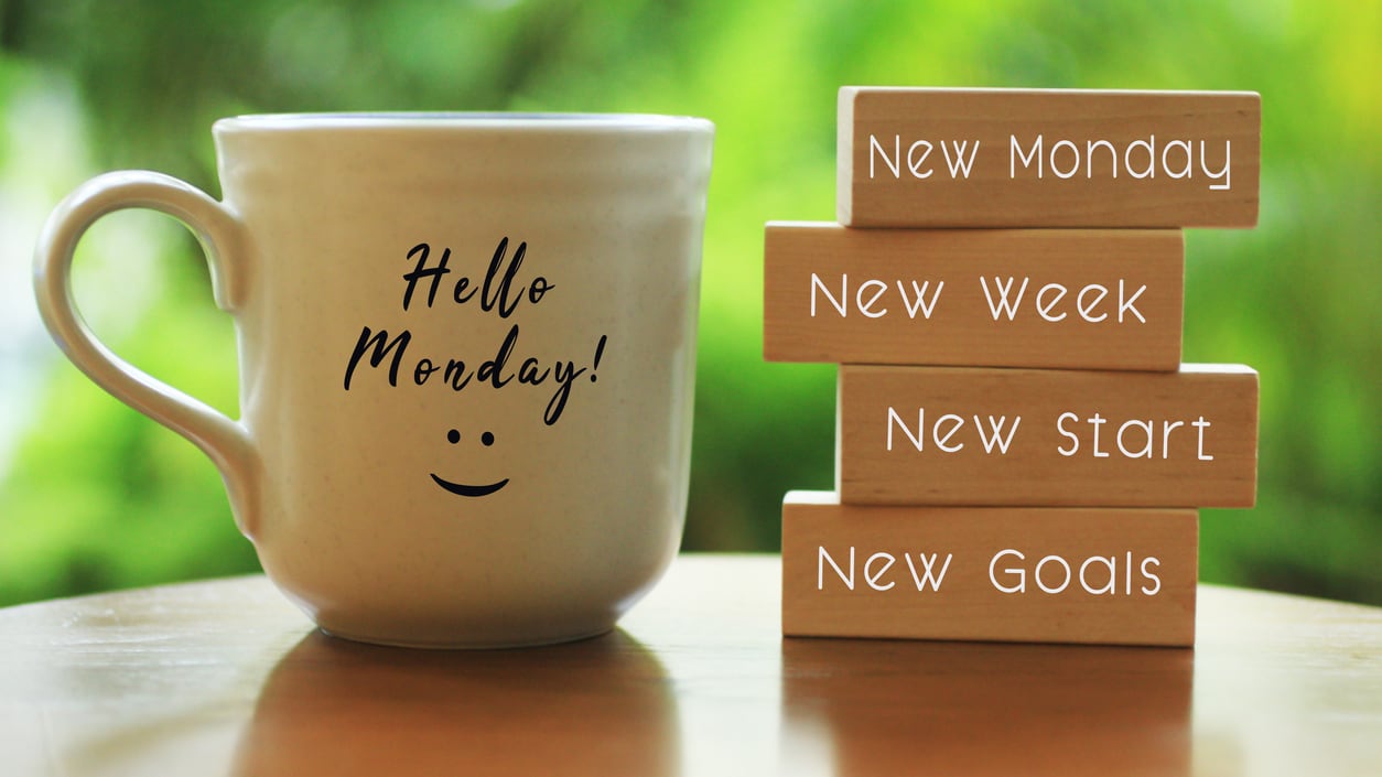 A mug with the words hello monday next to a stack of wooden blocks.