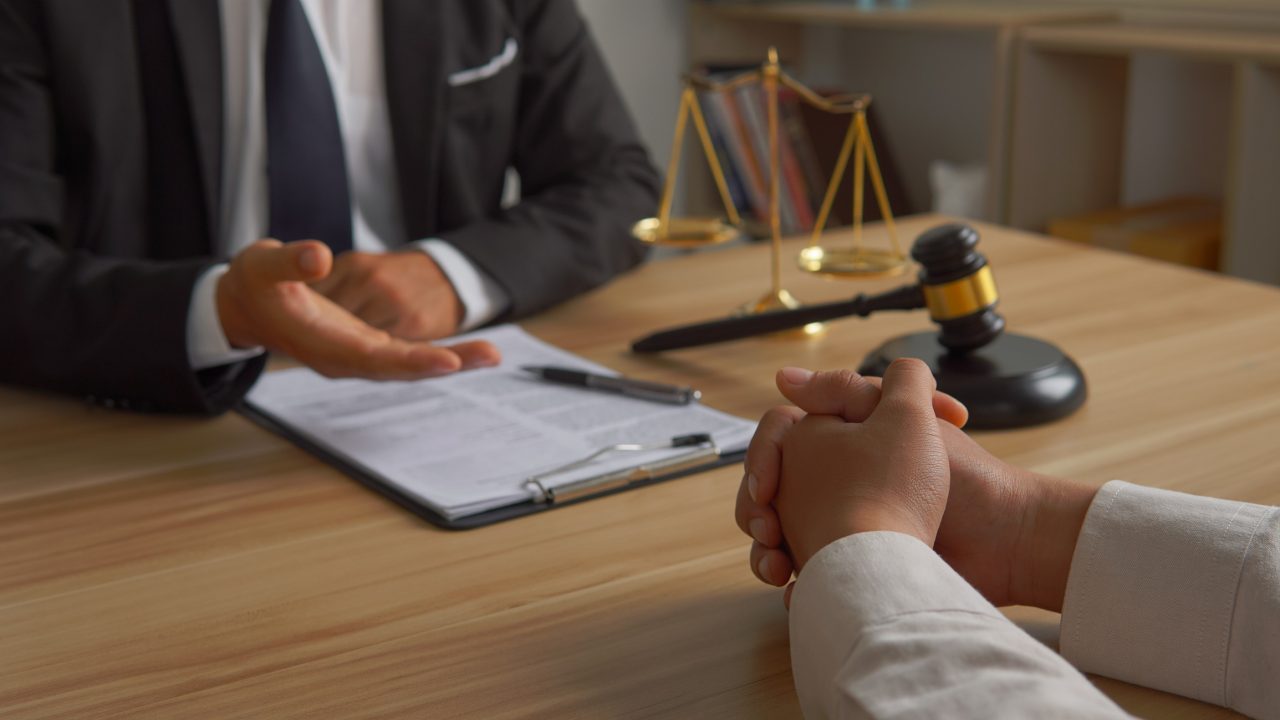 A client speaks with a lawyer at a table next to a gavel. 