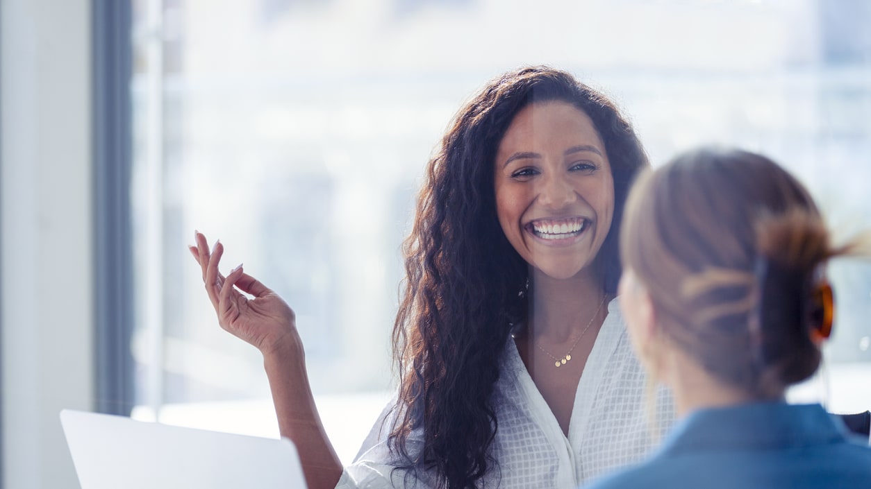 Two women sitting in an office talking to each other.