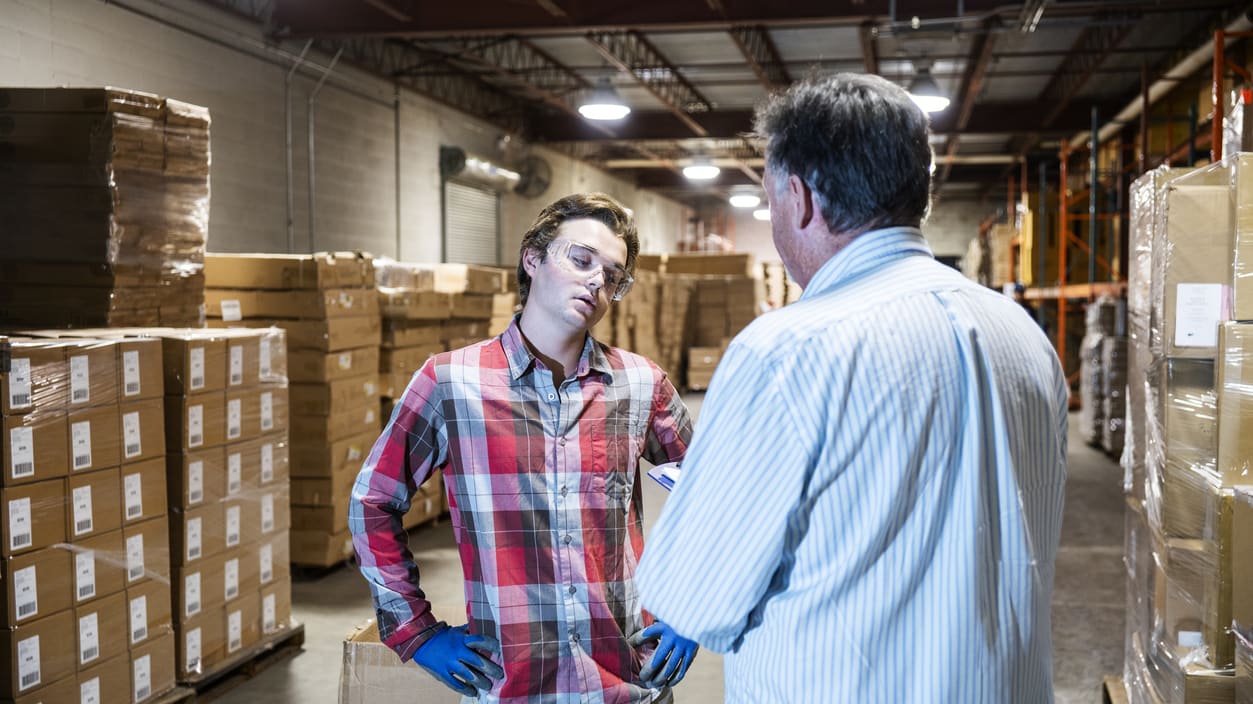 Two men in a warehouse talking to each other.