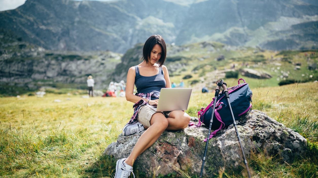 A woman is sitting on a rock and using a laptop.