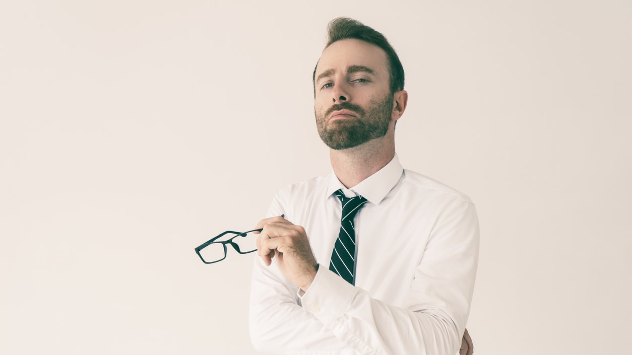 A man in a white shirt and tie is holding a pair of glasses.