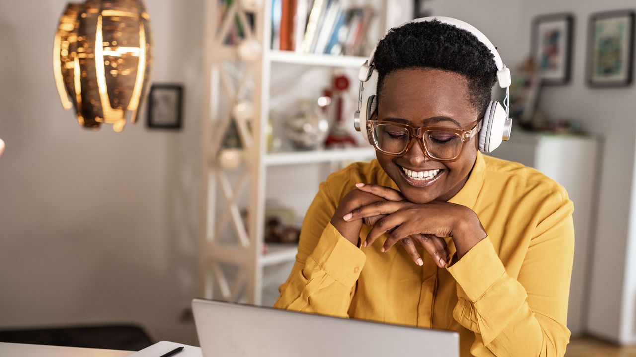 A woman wearing headphones is sitting at a desk with a laptop.