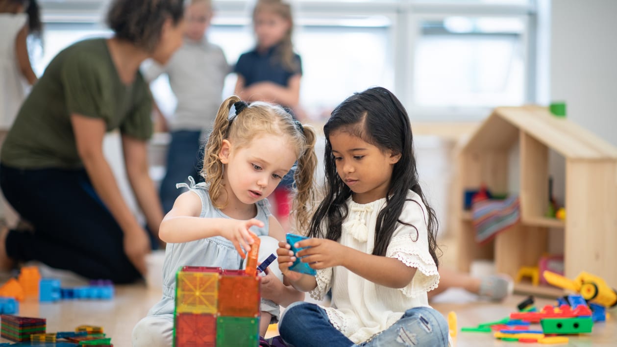 Two young girls playing with blocks in a classroom.