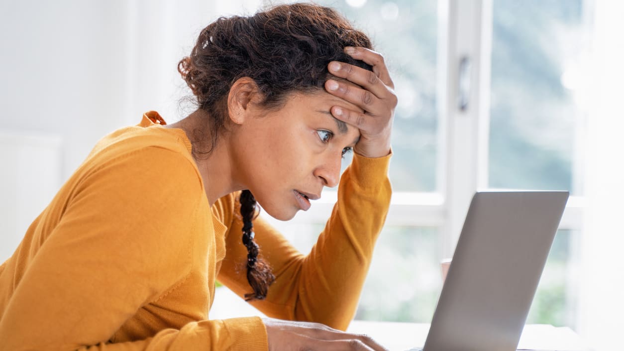 A woman is looking at her laptop with her hand on her head.