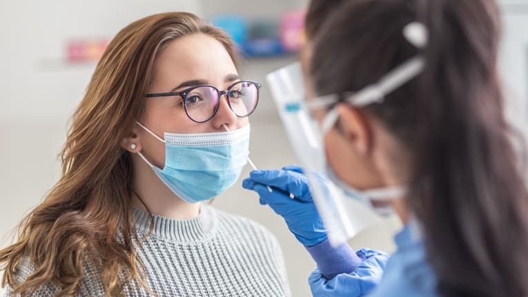 A woman wearing a surgical mask is being examined by a dentist.