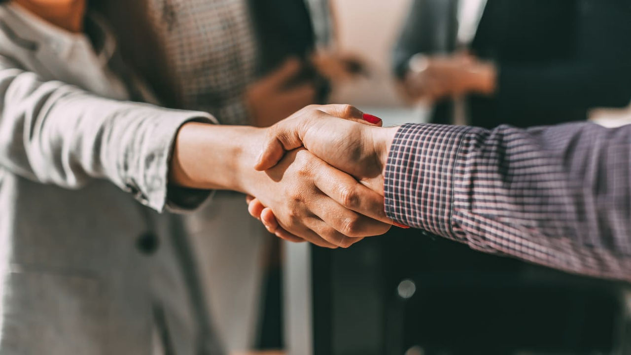 Two business people shaking hands in front of a group of people.