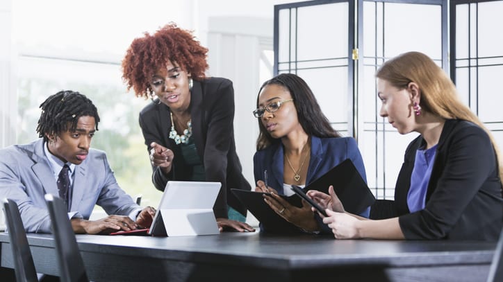 A group of business people sitting around a table looking at a laptop.