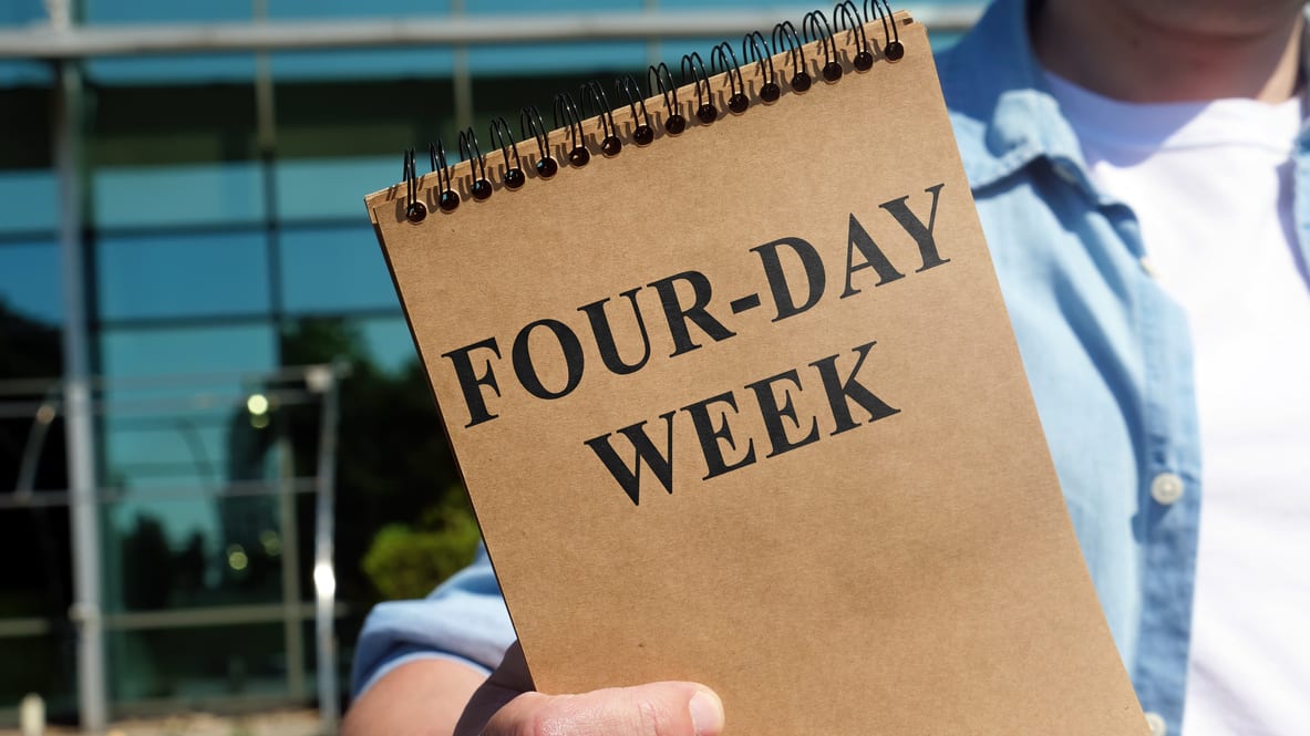 A man holding a notebook that says four day week.