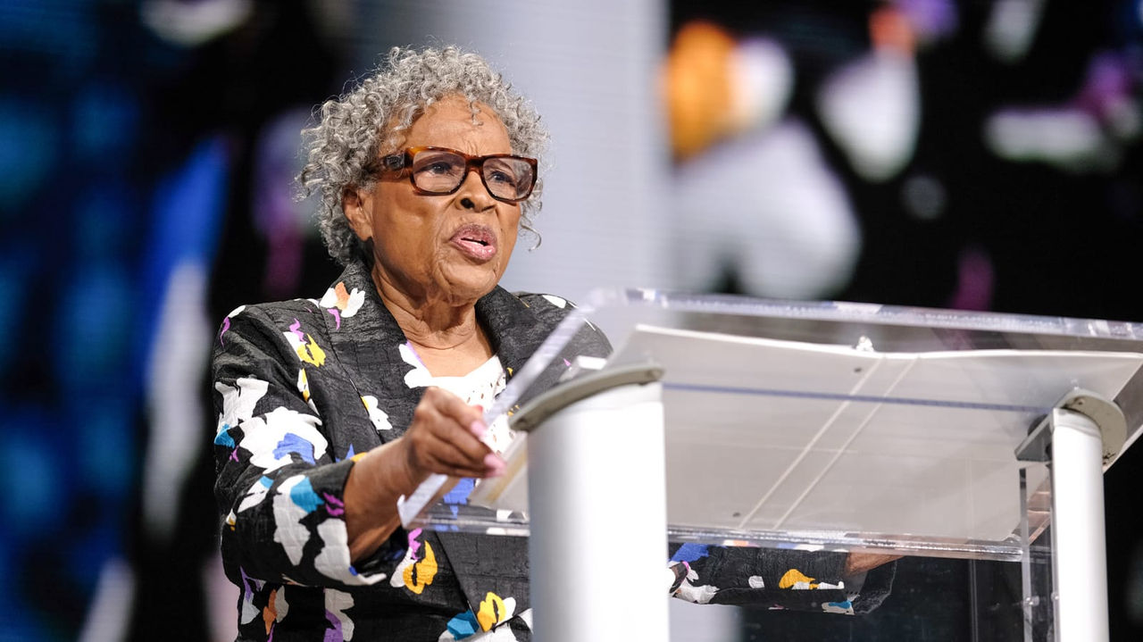 An older woman giving a speech at a podium.
