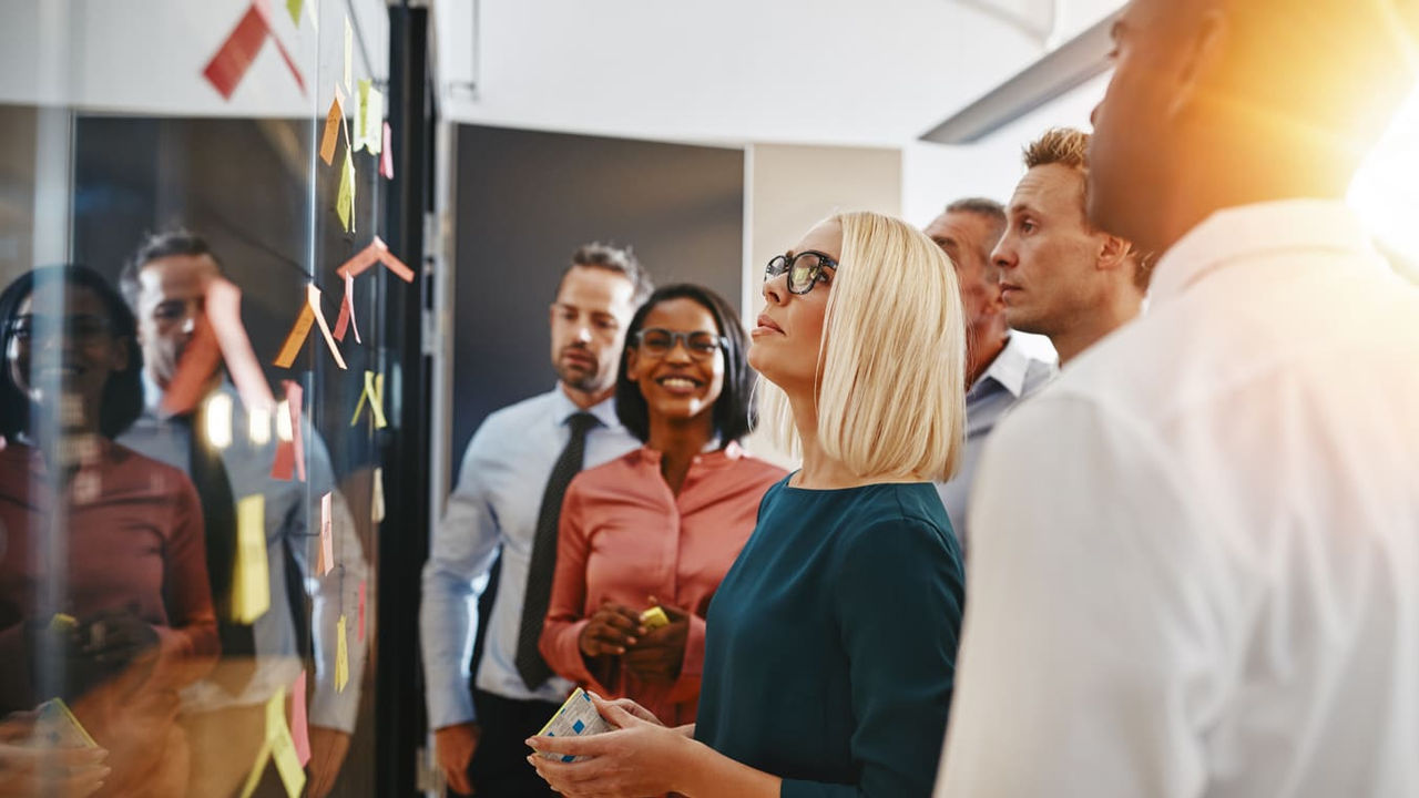 A group of business people looking at a board with sticky notes on it.