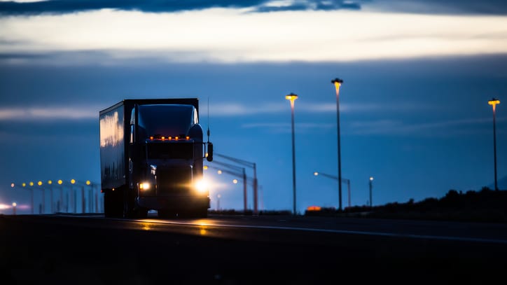 A semi truck driving down a highway at dusk.