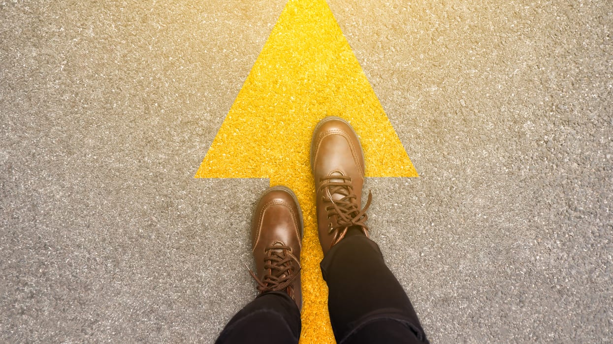 A person's feet standing on a yellow arrow.