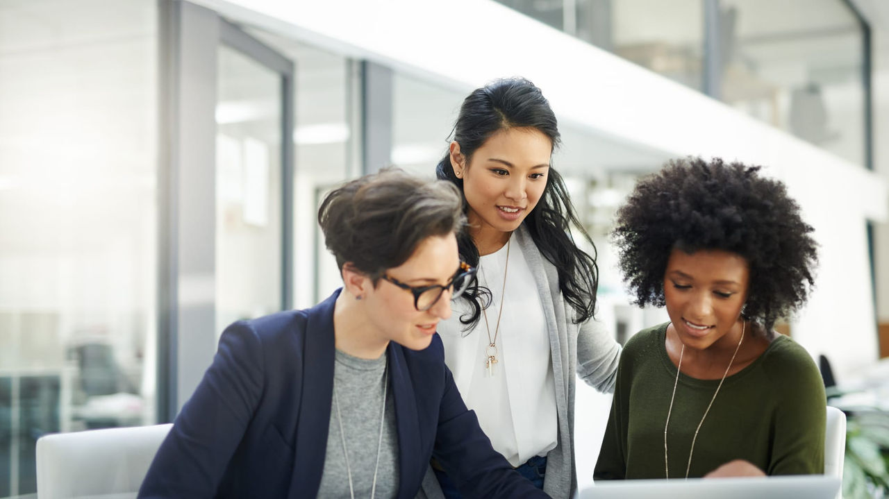 Three business women looking at a laptop in an office.