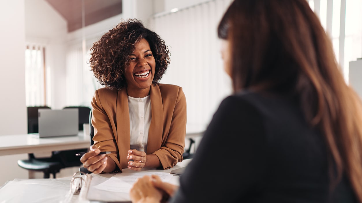 Two women talking at a desk in an office.