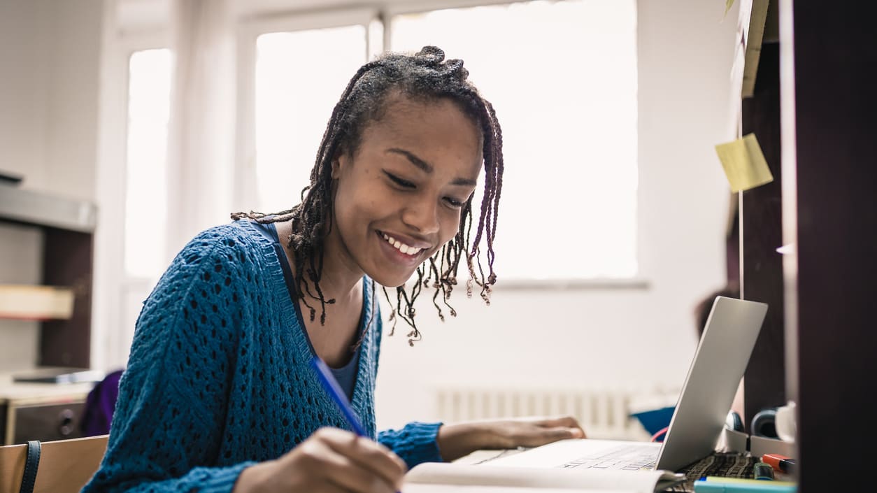 A young woman writing on a laptop in a library.