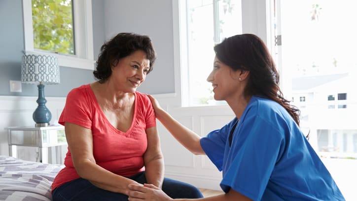 A nurse is talking to an older woman on a bed.