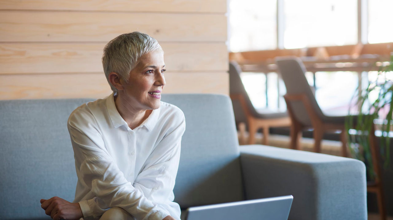 An older woman sitting on a couch using a laptop.