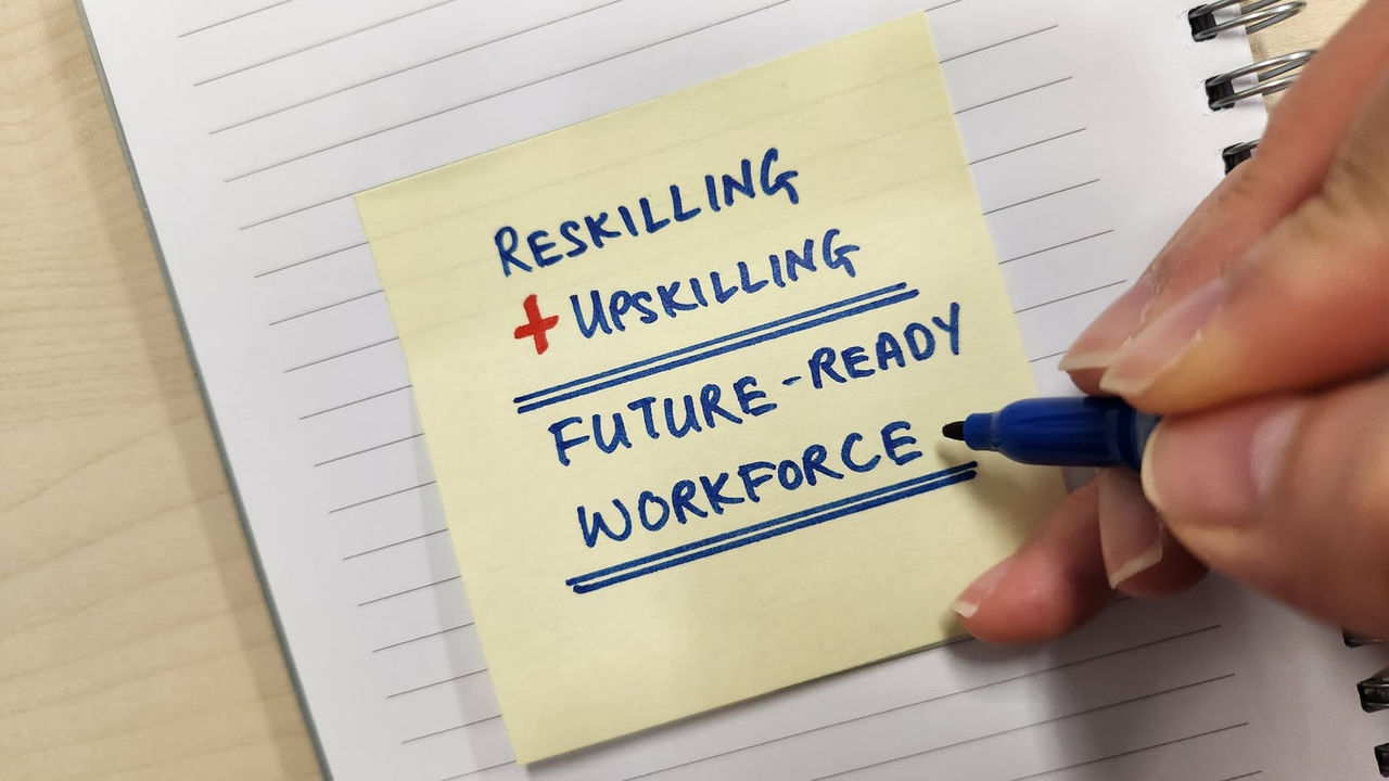 A person writing on a sticky note that says reskilling future ready workforce.