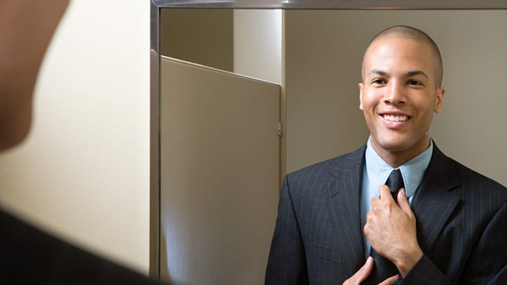 A man in a suit adjusting his tie in front of a mirror.