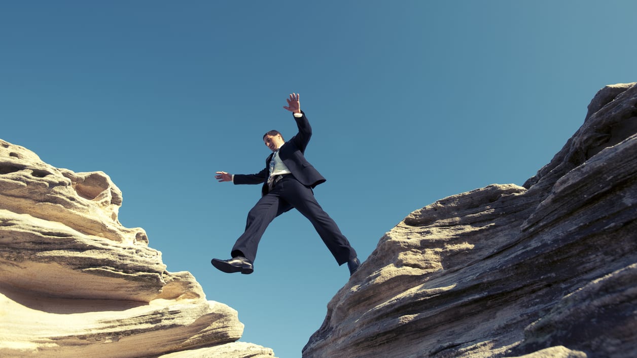A businessman jumping over a cliff.