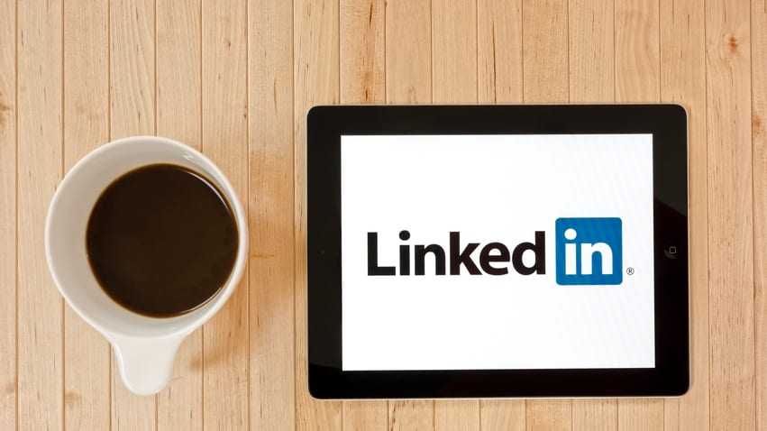 An iPad with the linkedin logo next to a cup of coffee.