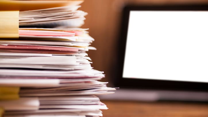 A stack of papers in front of a laptop computer.