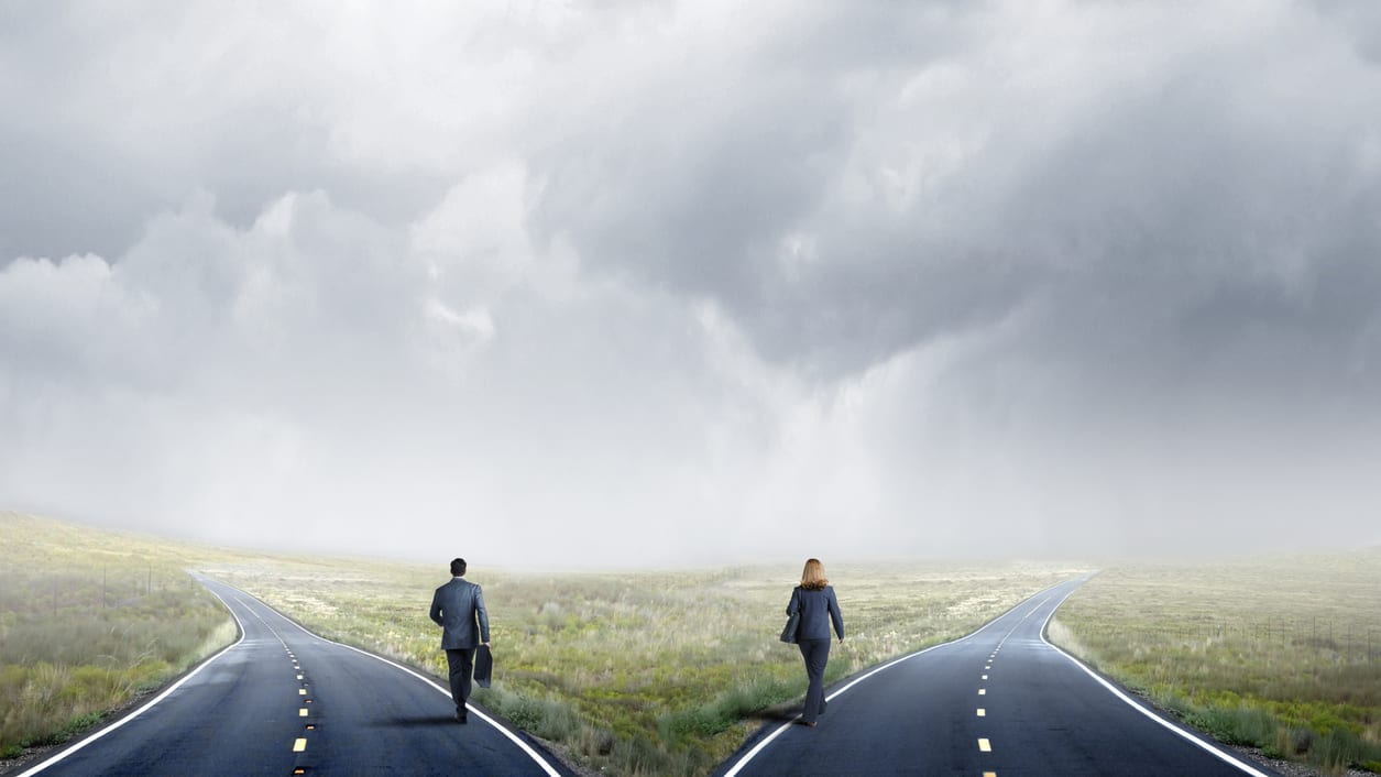Two business people walking down an empty road under a stormy sky.