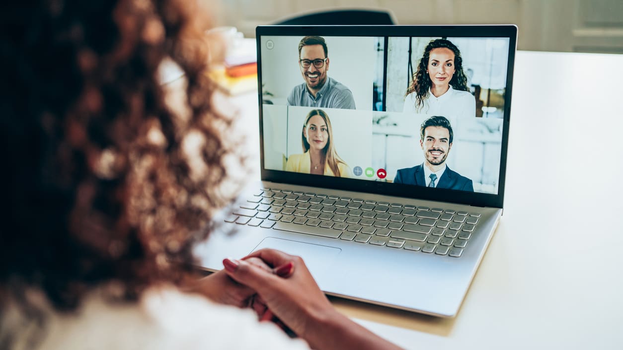 A woman is using a laptop with several people on a video call.