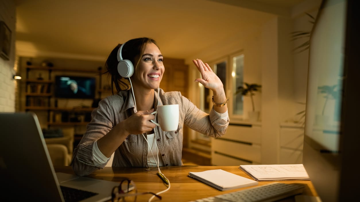 A woman is sitting at her desk with headphones on and a cup of coffee.