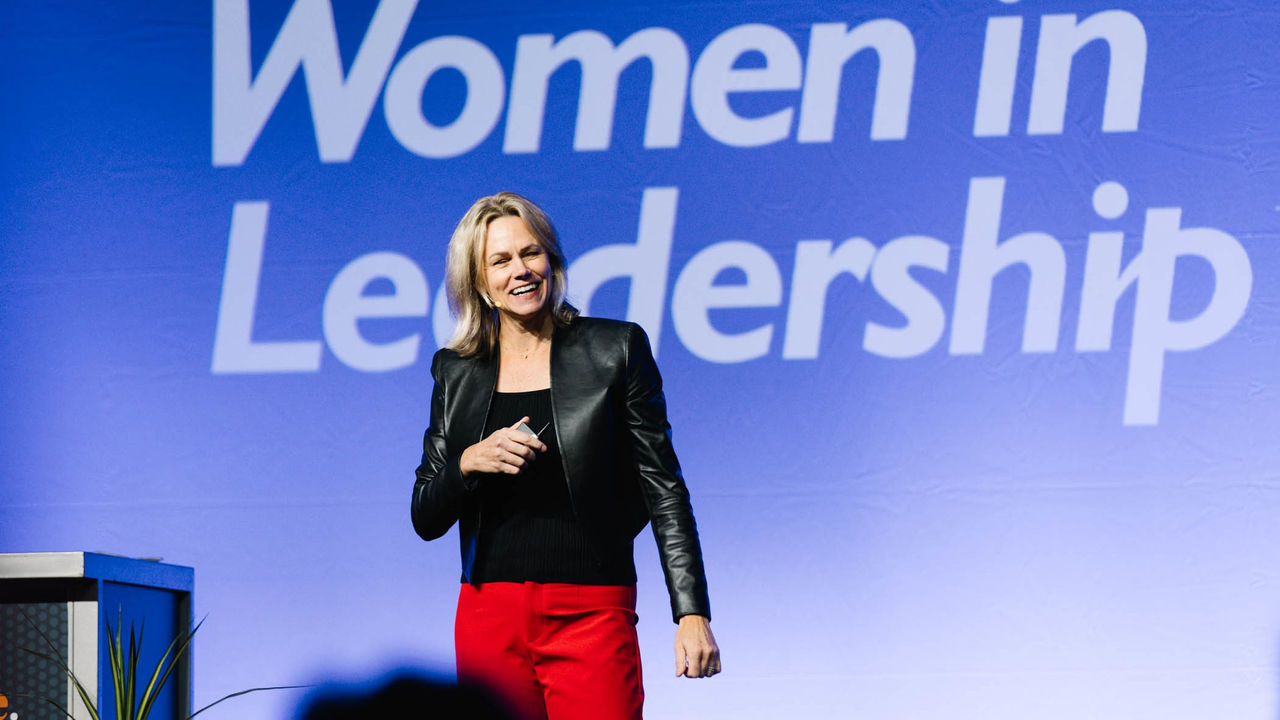 A woman standing in front of a sign that says women in leadership.