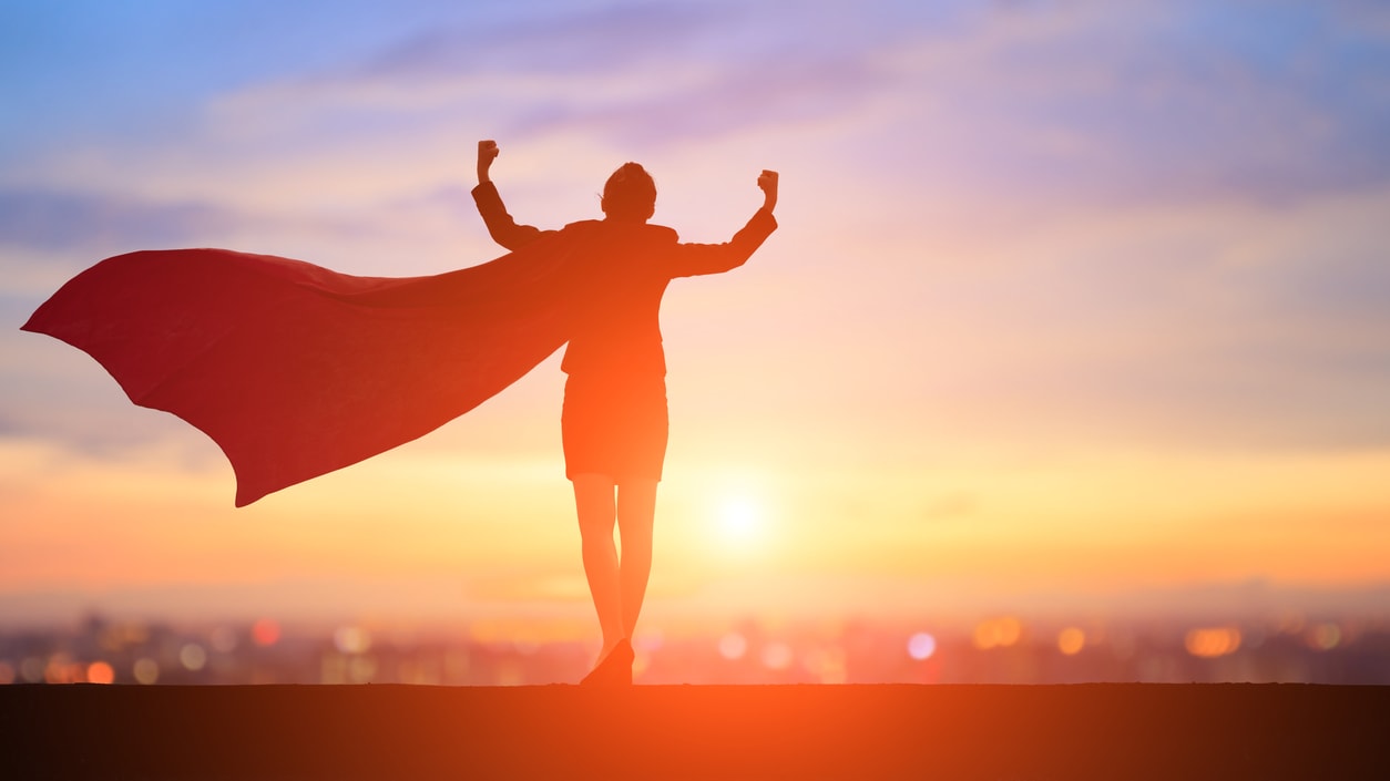 Silhouette of a woman with a red cape standing on top of a hill at sunset.