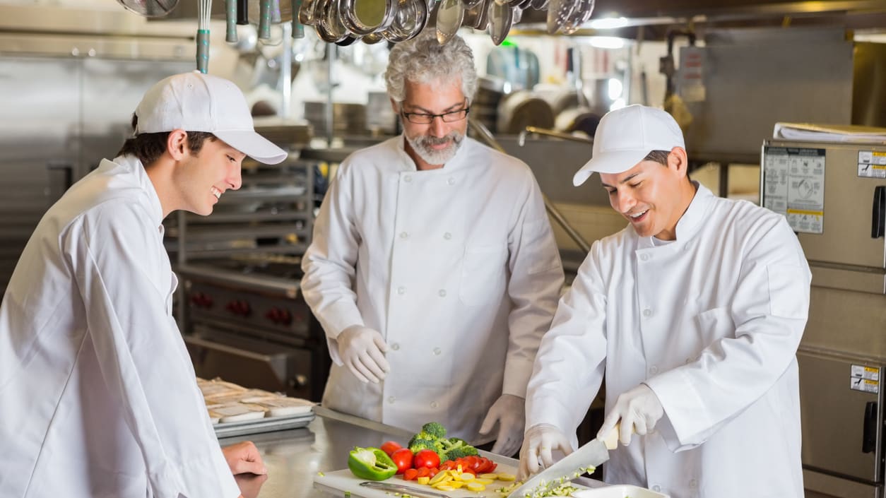 Three chefs preparing food in a commercial kitchen.