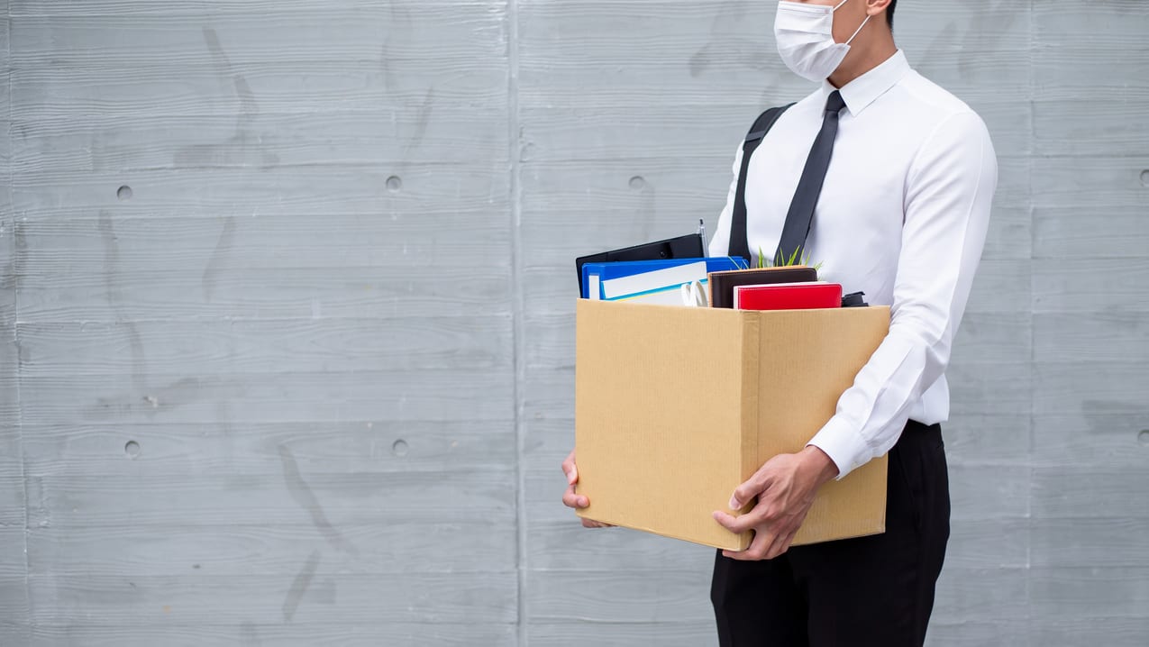 A businessman wearing a face mask holding a box.