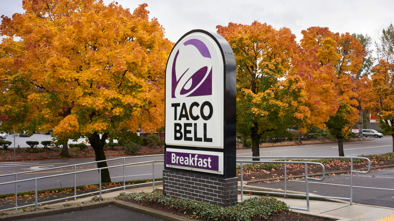 A Taco Bell sign is parked in front of trees.