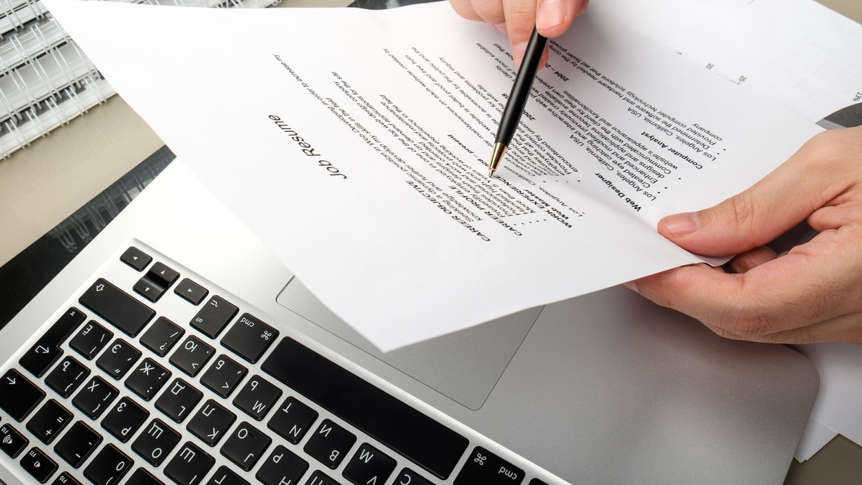 A person writing on a piece of paper in front of a laptop.