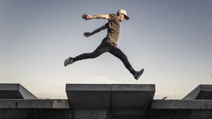 A man is jumping over a concrete ramp.