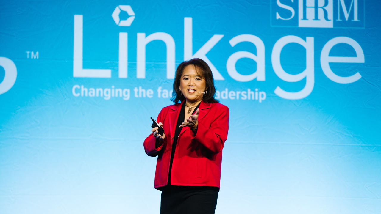 A woman in a red jacket standing in front of a linkage sign.