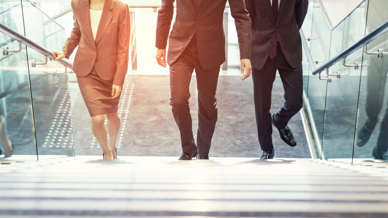 Three business people walking down an escalator.