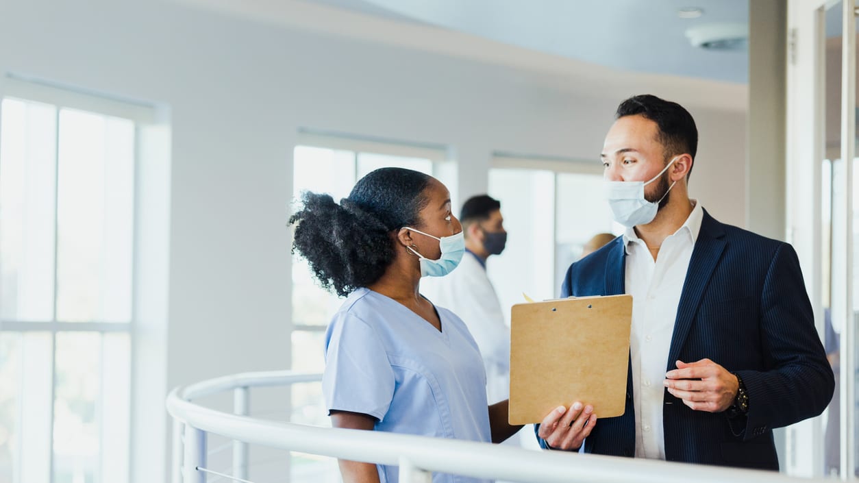 A nurse is talking to a patient in a hospital hallway.