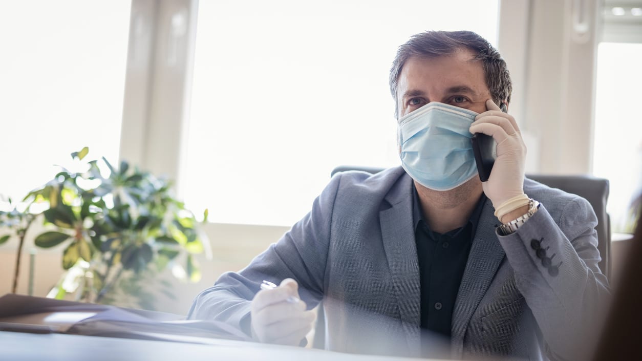 A businessman wearing a surgical mask while talking on the phone.