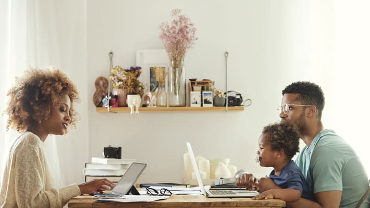 A woman and man sitting at a table working on laptops with their child.