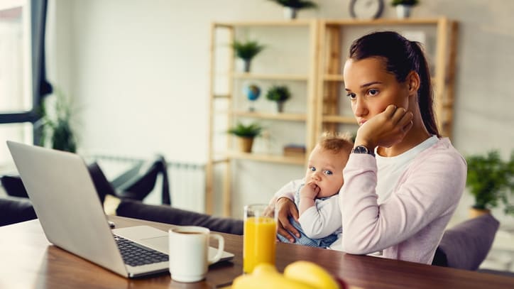 A woman sitting at a table with a baby in front of her laptop.