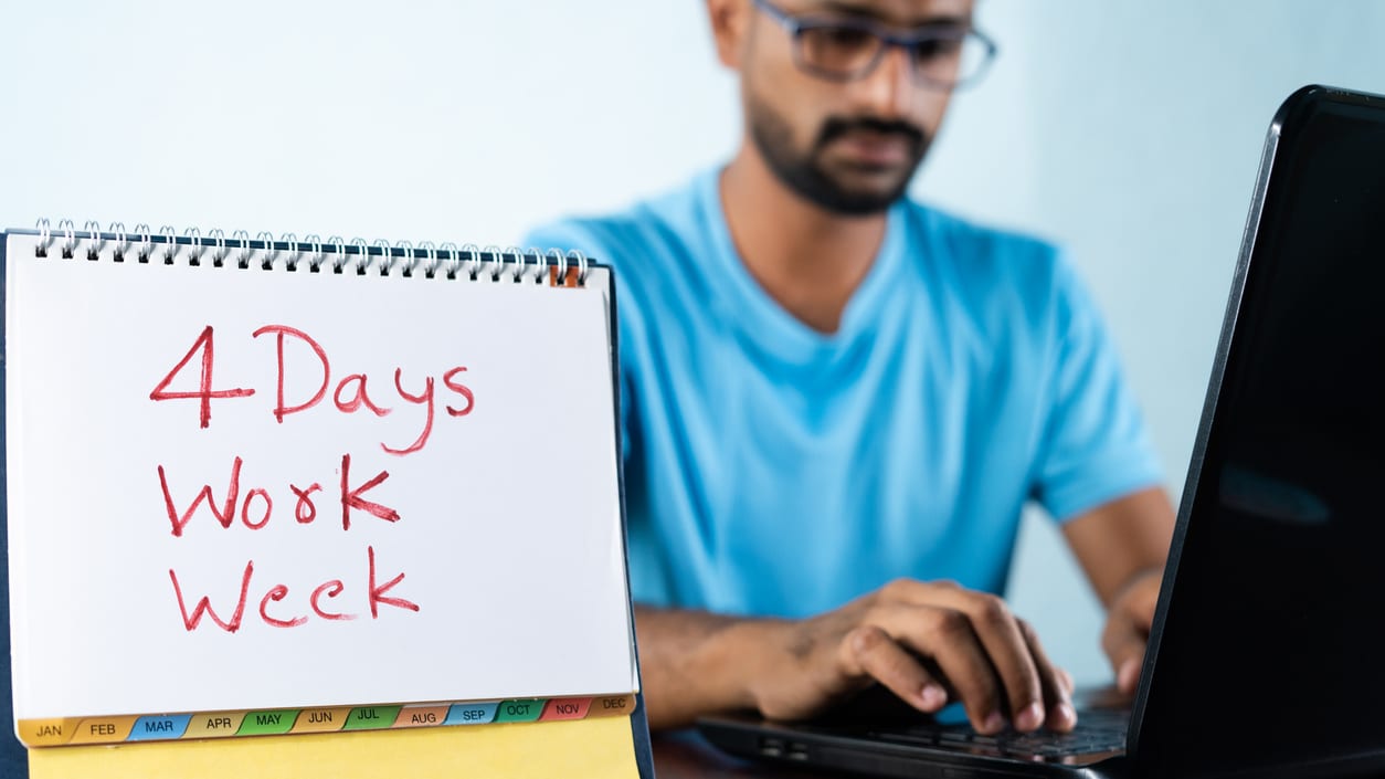 A man working on a laptop with a sign that says 4 days work week.