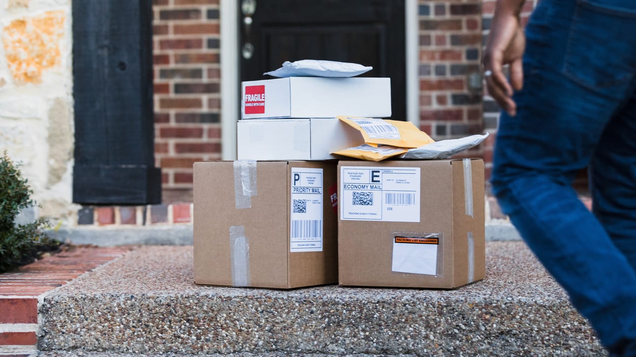 A man is walking down the steps of a house with a stack of boxes.